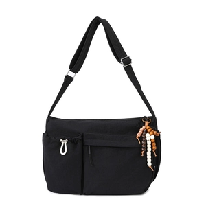 Close-up of black nylon crossbody bag featuring side drawstring pocket and wood bead charm