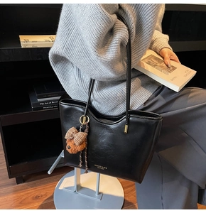 Detail of black faux leather tote bag with gold logo and brown puppy plush pendant
