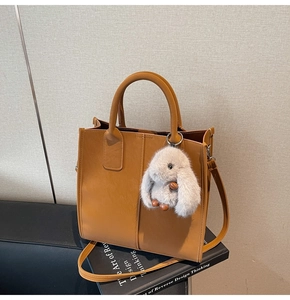 Close-up of caramel brown tote bag featuring vertical stitching and a plush rabbit charm