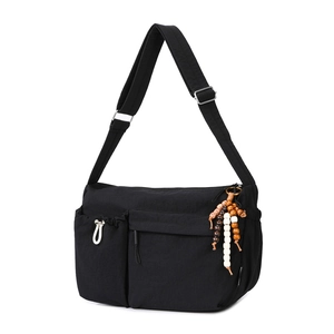 Detail of black multi-pocket crossbody bag featuring nylon fabric and wooden bead tassel