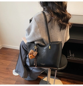 Detail of black wax leather tote bag with bear charm shown from a side-view on a model