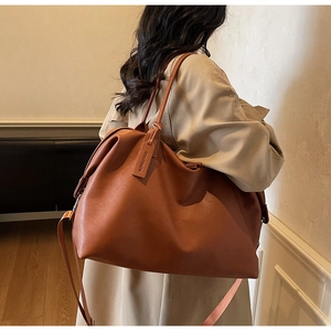 Detailed view of brown leather tote bag showing crossbody strap and luxury brand hangtag