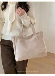 Close-up of beige suede tote bag with embossed logo and minimalist retro texture