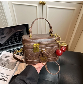 Brown quilted vintage box bag with cherry charm detail on a laptop and books background