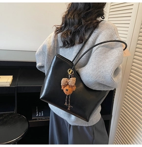 Detail of black faux leather tote bag with long straps and a plush bear pendant