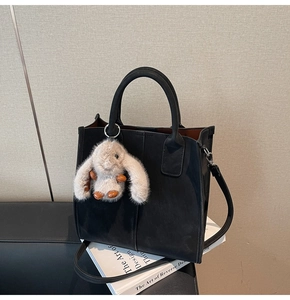 Detail of black leather tote bag featuring a plush rabbit charm and crossbody strap