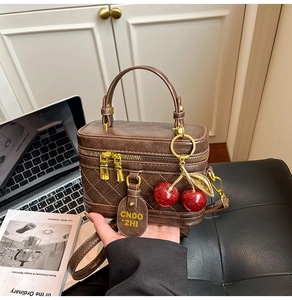 Detail of brown quilted leather box bag with gold zipper and red cherry charm