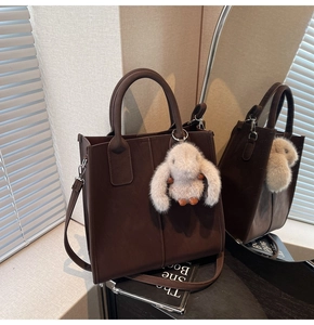 Detail of coffee brown matte tote bag with shoulder strap and plush rabbit charm accessory