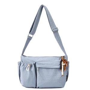Close-up of the light blue nylon crossbody bag featuring a front pocket and beaded tassel