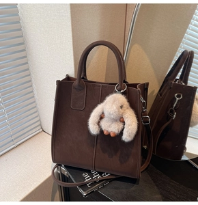 Detail of dark brown leather tote bag with plush bunny charm and adjustable shoulder strap