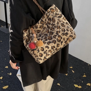 Detail of leopard print plush tote bag with brown woven handles and colorful pom-poms