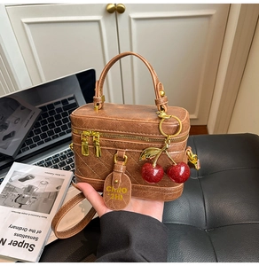 Detail of vintage brown quilted leather vanity bag with cherry charm and gold zippers