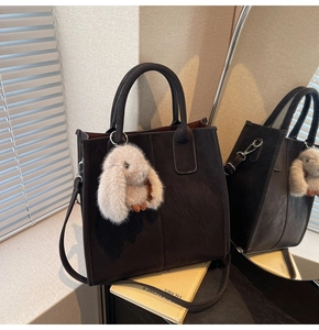 Detail of dark brown matte tote bag with plush rabbit charm and stitching details