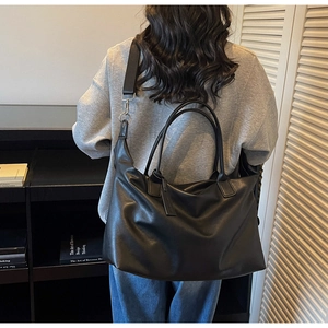 Detail of a large black leather tote bag featuring dual handles and a detachable shoulder strap