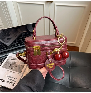 Close-up of burgundy leather box bag featuring quilted side details and cherry charm