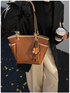 Detailopname van een tweekleurige tote bag met klaverhanger in een herfstachtige setting