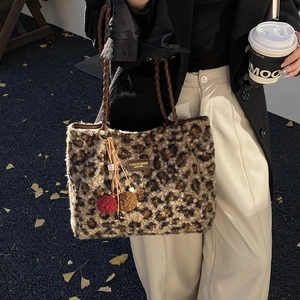 Detail of leopard print plush tote bag featuring braided handles and fluffy pompom charms