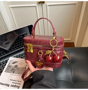 Close-up of burgundy quilted box bag with gold hardware and cherry charm on desk