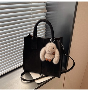 Detail of black leather tote bag with gray plush bunny charm and adjustable strap