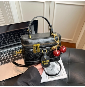 Detail of black quilted box bag with red cherry charm and gold-tone zippers