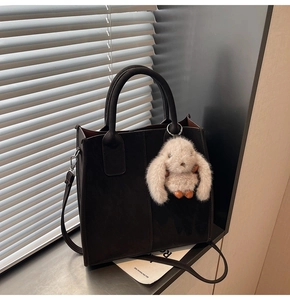 Detail of black tote bag with plush rabbit charm and adjustable shoulder strap