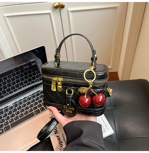 Close-up of black quilted box bag with dual gold zippers and cherry sequins charm