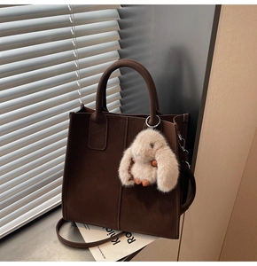 Detail of dark brown tote bag with plush rabbit pendant on a windowsill with blinds