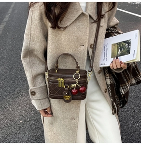 Detail of coffee brown quilted leather crossbody box bag with red cherry charm