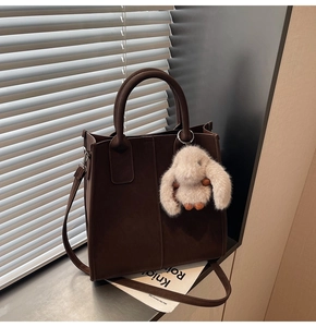 Detail view of coffee brown tote bag with fuzzy white rabbit charm on side