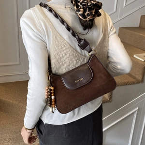 Détail du sac bandoulière rétro en daim marron avec bandoulière tressée et pompon