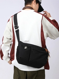 Black nylon crossbody messenger bag with adjustable strap and side beaded charm detail