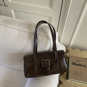 Detail of dark brown retro shoulder bag with large silver buckle on white sofa