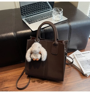Brown leather square tote bag with cute plush rabbit charm on a wooden background