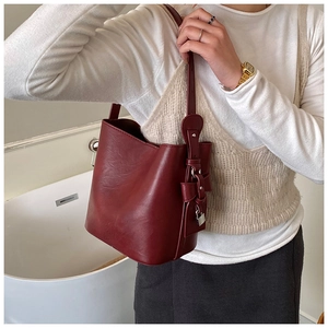 Detail of burgundy leather bucket bag with silver lock charm and adjustable shoulder strap