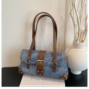 Detail of blue denim shoulder bag with brown leather trim and silver metal rivet studs