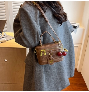 Detail of a brown quilted box bag with a gold zipper and a red cherry charm accessory