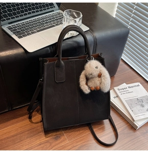 Close-up of deep brown leather tote bag with a plush bunny charm on an office desk