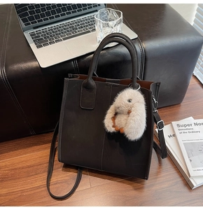 Detail of taupe leather tote bag with plush bunny charm and red-brown lining