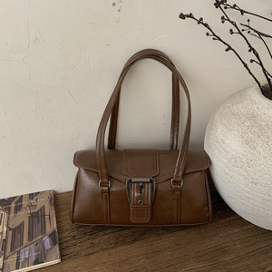 Close-up of vintage brown PU leather bag with large metal buckle on rustic wood