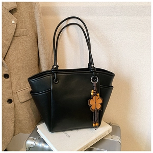 Detailopname van zwarte leren shopper met bloemenhanger tegen stijlvolle grijze kostuumachtergrond