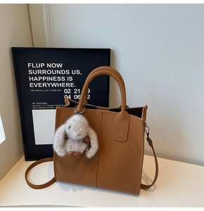 Detail of caramel leather tote bag showing fine stitching and plush rabbit charm