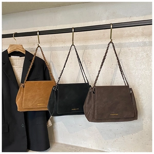 Three retro suede chain bags in brown, black and coffee hanging on a metallic display rack