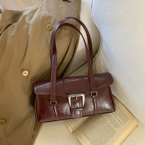 Detail of a burgundy vintage oil wax shoulder bag with a large silver buckle on a trench coat