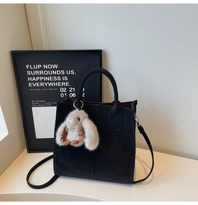 Detail of matte black tote bag with gray plush rabbit charm and crossbody strap