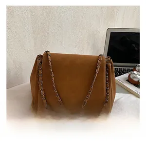 Detail of a brown suede chain bag with minimalist logo next to a laptop and accessories