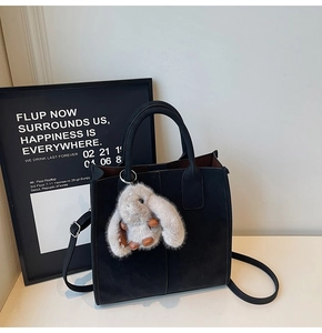 Detail of black matte leather tote bag with plush rabbit charm and adjustable strap
