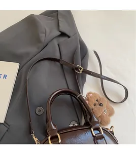Detail of dark brown leather Boston bag with gold hardware and plush bear charm