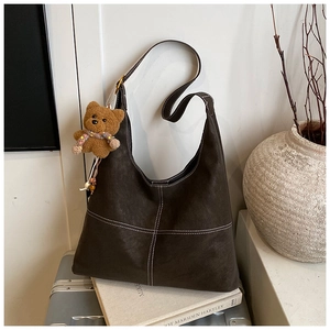 Dettaglio borsa hobo in pelle scamosciata marrone scuro con cuciture bianche e orsetto