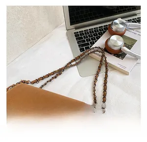 Detail of a brown leather shoulder bag featuring a metal chain and woven leather strap