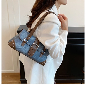 Detail of blue denim shoulder bag with brown leather trim and silver studs on model
